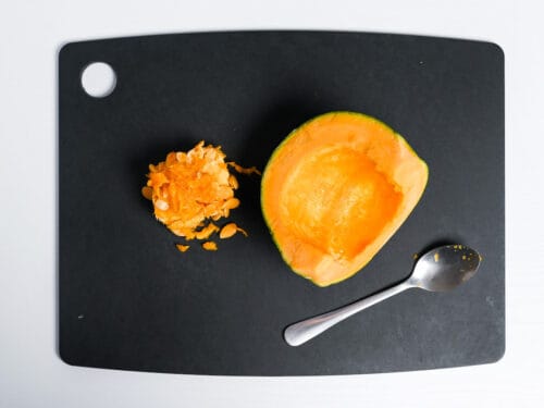 Kabocha Japanese squash on a black chopping board with seeds scooped out