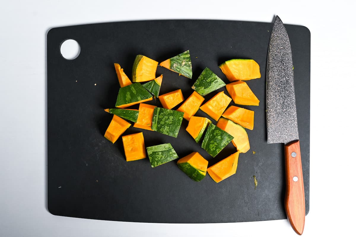 Kabocha Japanese squash cut into bitesize pieces on a black chopping board