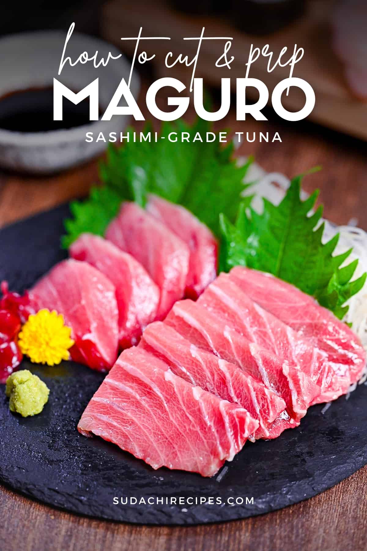 fresh pieces of sashimi-grade tuna (maguro) on a round slate plate with shiso leaves, shredded daikon, wasabi and seaweed
