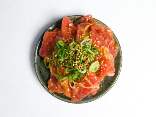 miso marinated tuna sashimi on a green plate topped with chopped green onion