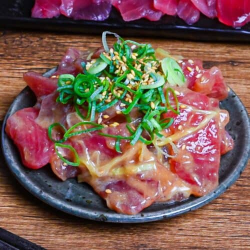 Tuna Sashimi (maguro) coated in a miso-based sauce topped with chopped green onions and sesame seeds served on a green plate