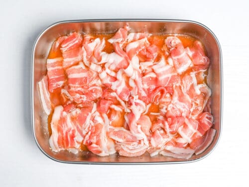 marinating thinly sliced pork belly in a metal container