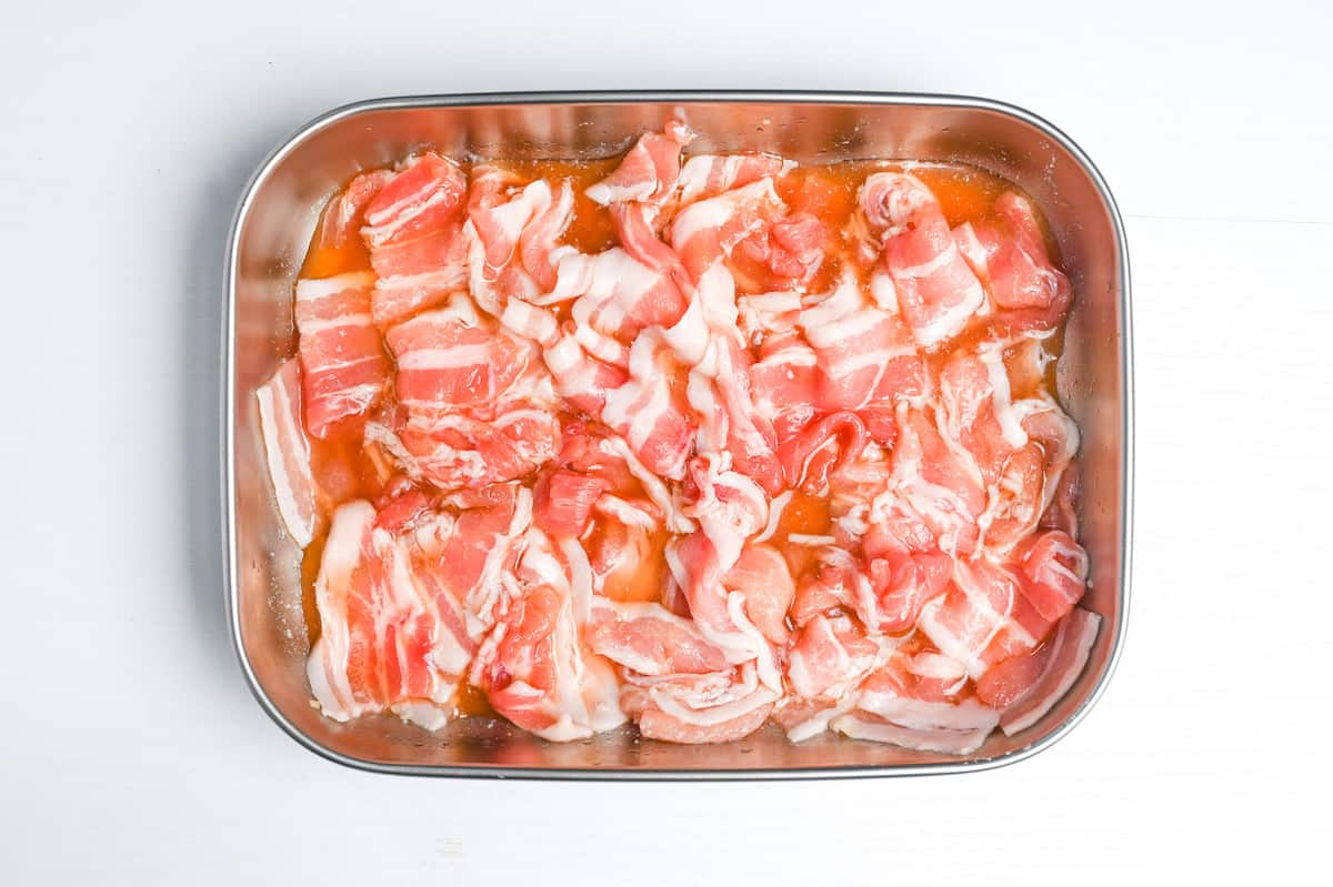 marinating thinly sliced pork belly in a metal container