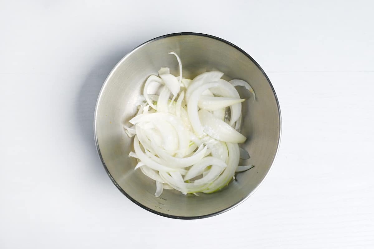salted sliced onions in a metal mixing bowl