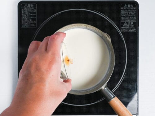pouring vanilla essence into milk and cream in a sauce pan