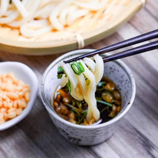 dipping cold udon noodles in mentsuyu (noodle dipping sauce) mixed with green onions