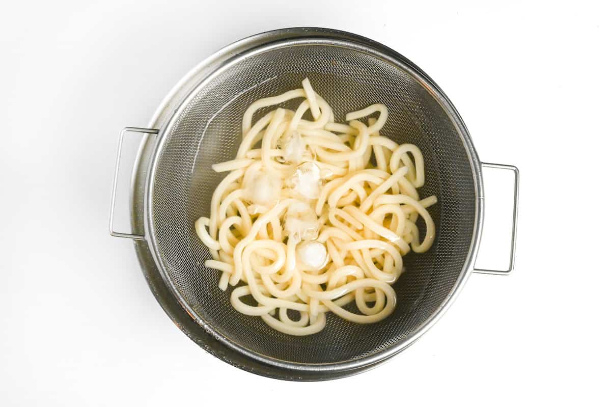 chilling cooked udon noodles with ice in a mesh sieve over a bowl of cold water
