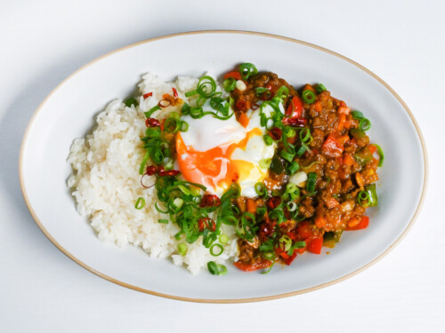 dry curry with rice topped with green onion, chili and green onion on an oval-shaped white plate with beige rim