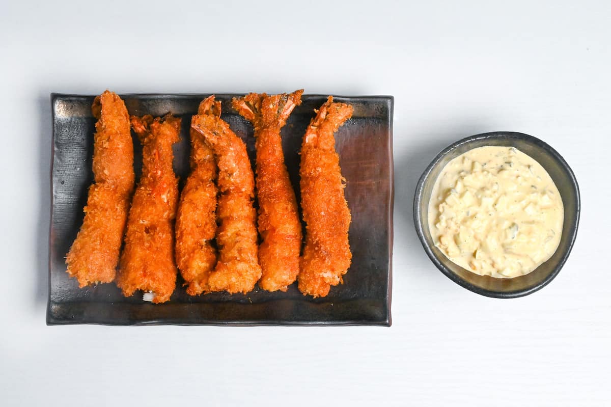 6 golden and crispy ebi fry on a plate next to a small bowl of homemade Japanese tartar sauce