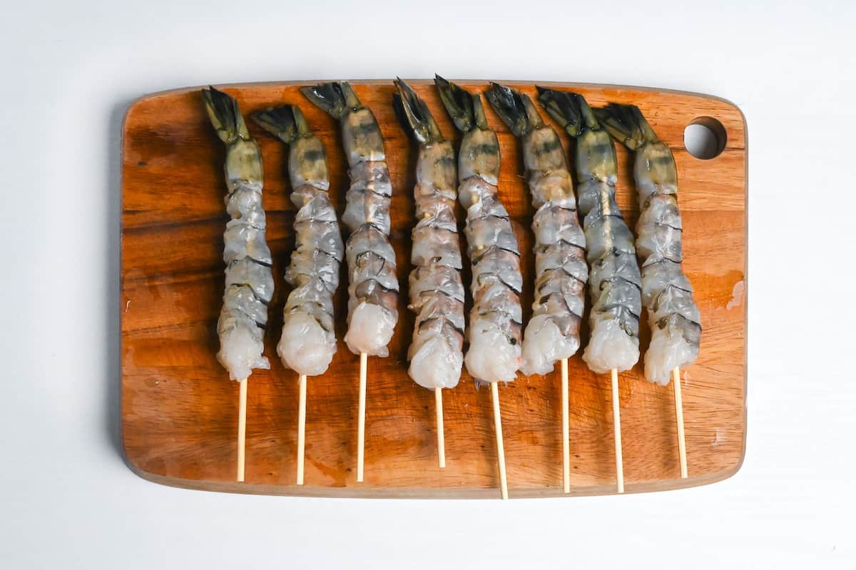 black tiger shrimp on bamboo skewers on a wooden chopping board