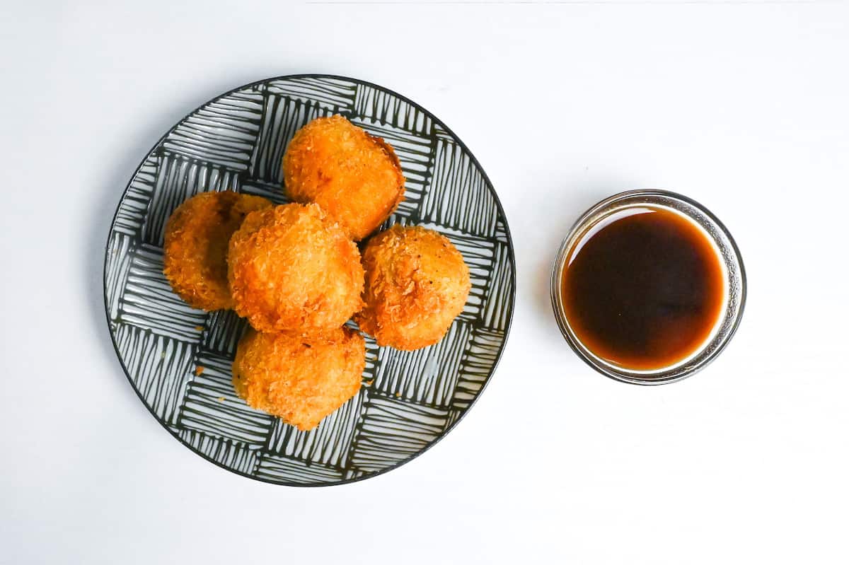 kabocha korokke stacked on a striped plate next to a small bowl of korokke dipping sauce