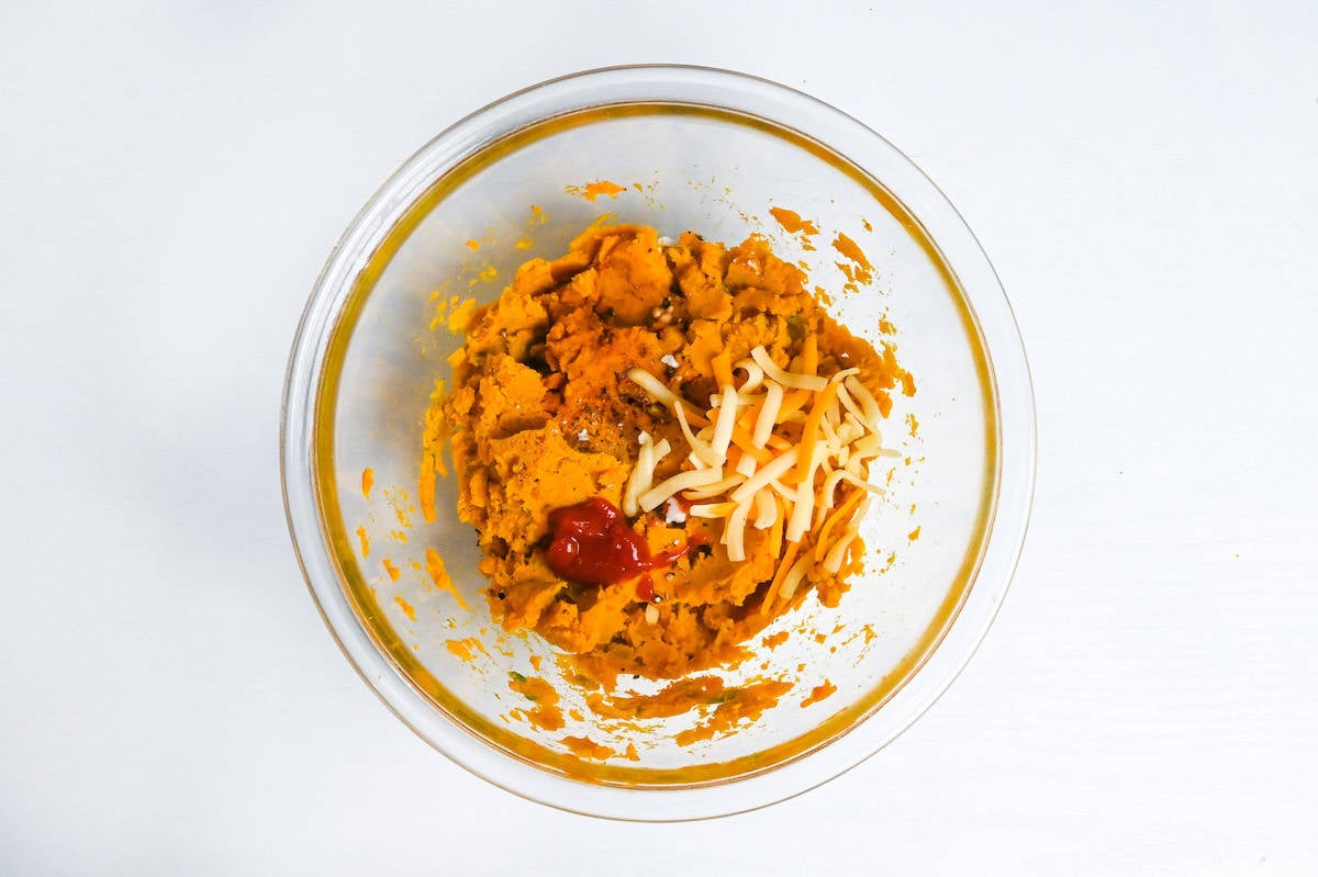 mashed kabocha in a glass bowl with seasonings, condiments and cheese