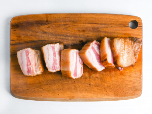 sealed pork belly cut into smaller pieces on a wooden chopping board