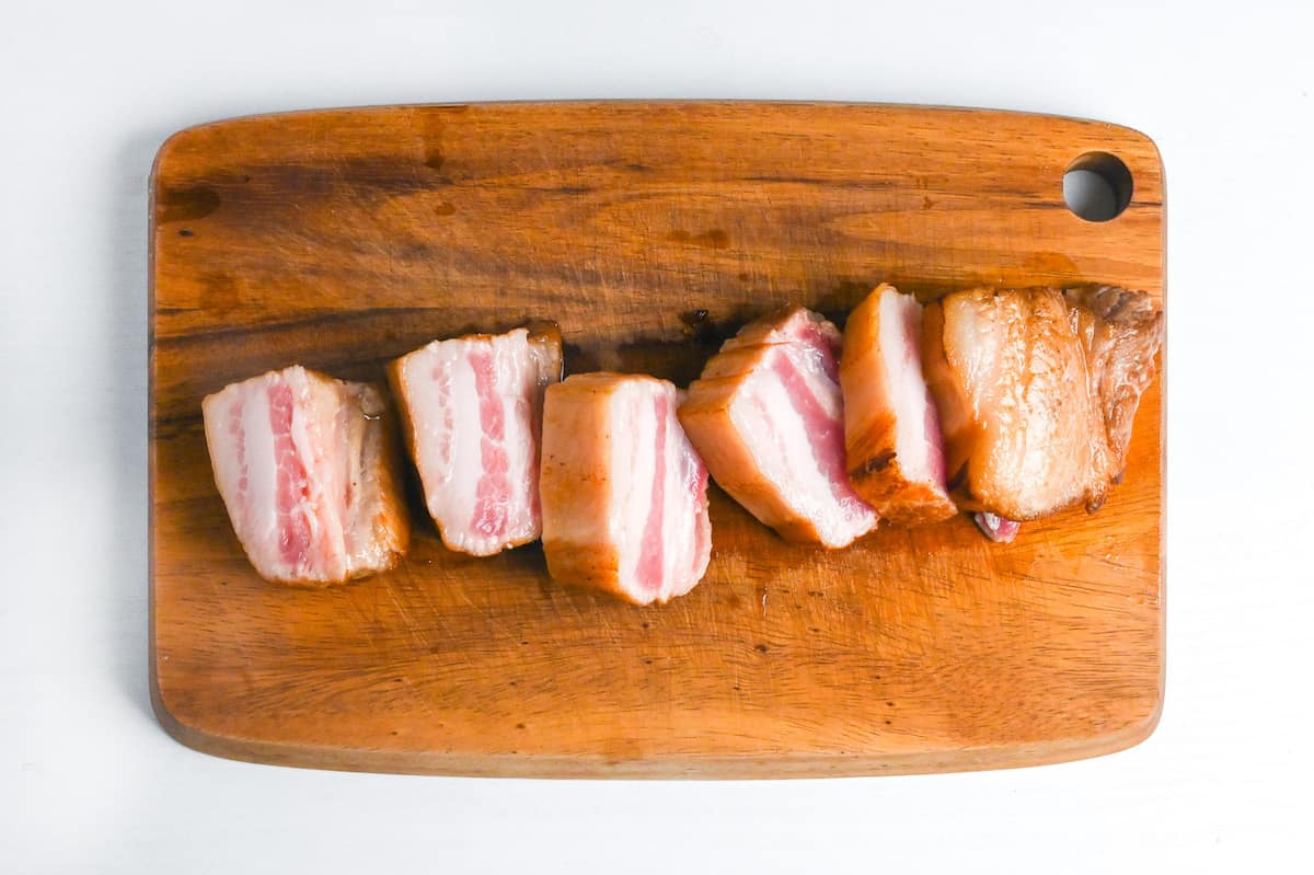 sealed pork belly cut into smaller pieces on a wooden chopping board