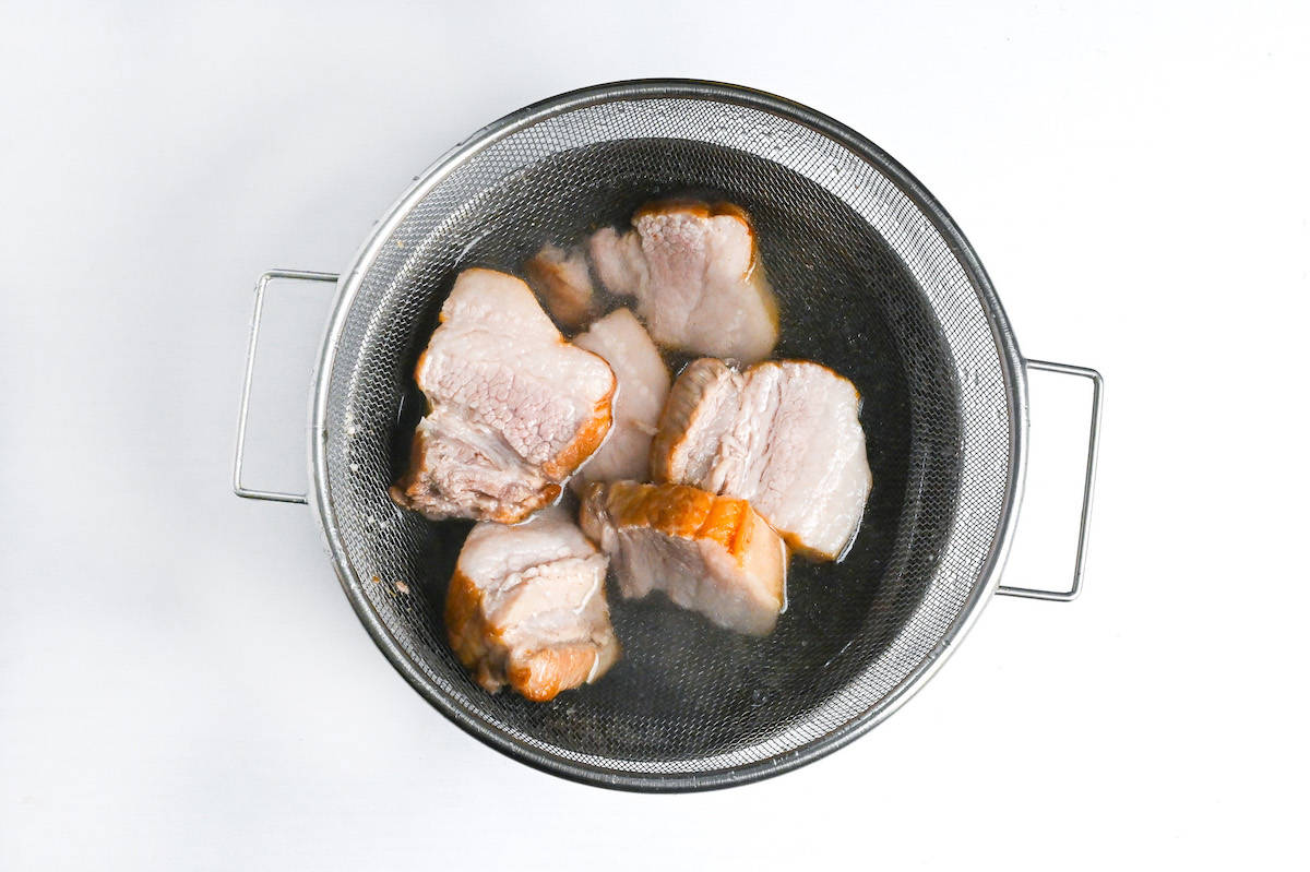 chunks of simmered pork belly in a mesh sieve