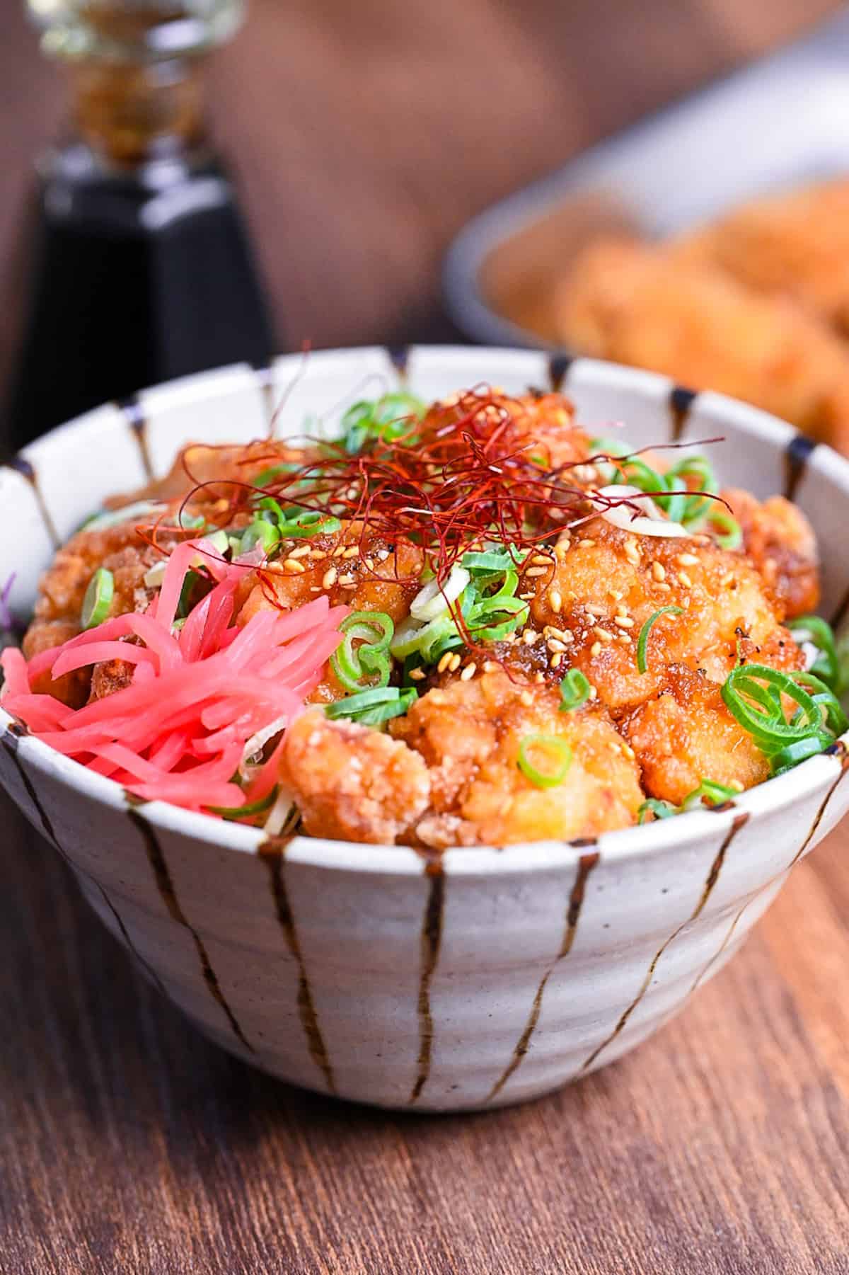 karaage don (Japanese fried chicken bowl) topped with sweet sauce, sesame seeds, chopped green onion, chili threads and pink pickled ginger.