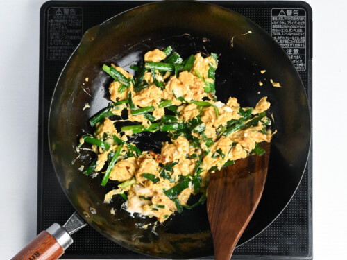 scrambling seasoned eggs and garlic chives in a wok
