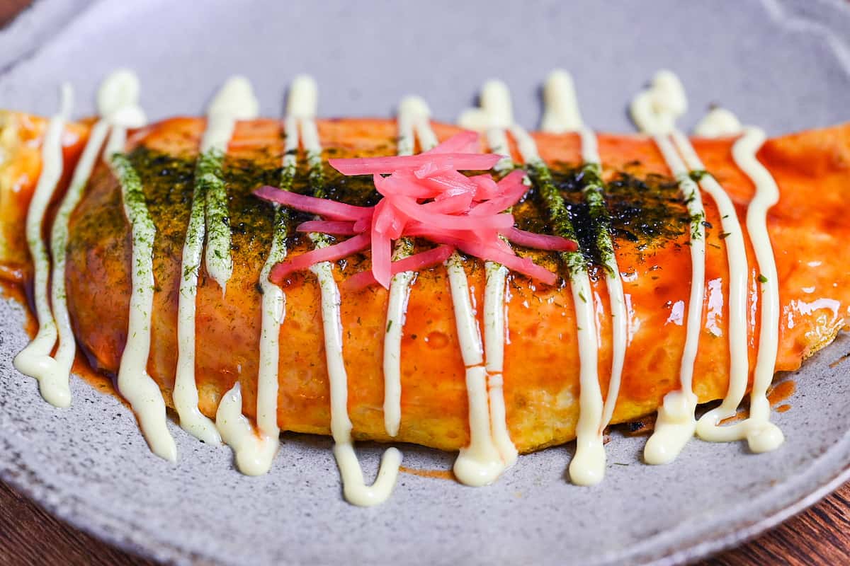 omusoba on a beige plate drizzled with okonomi sauce, Japanese mayo and topped with aonori and red pickled ginger