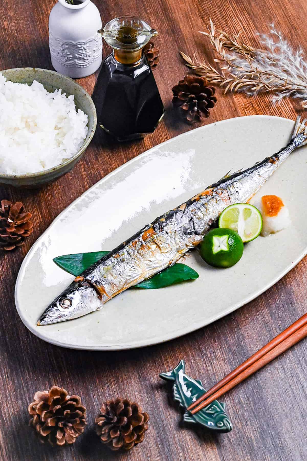 Grilled pacific saury (sanma no shioyaki) on a pale oval plate with grated daikon, sauce sauce and a halved sudachi