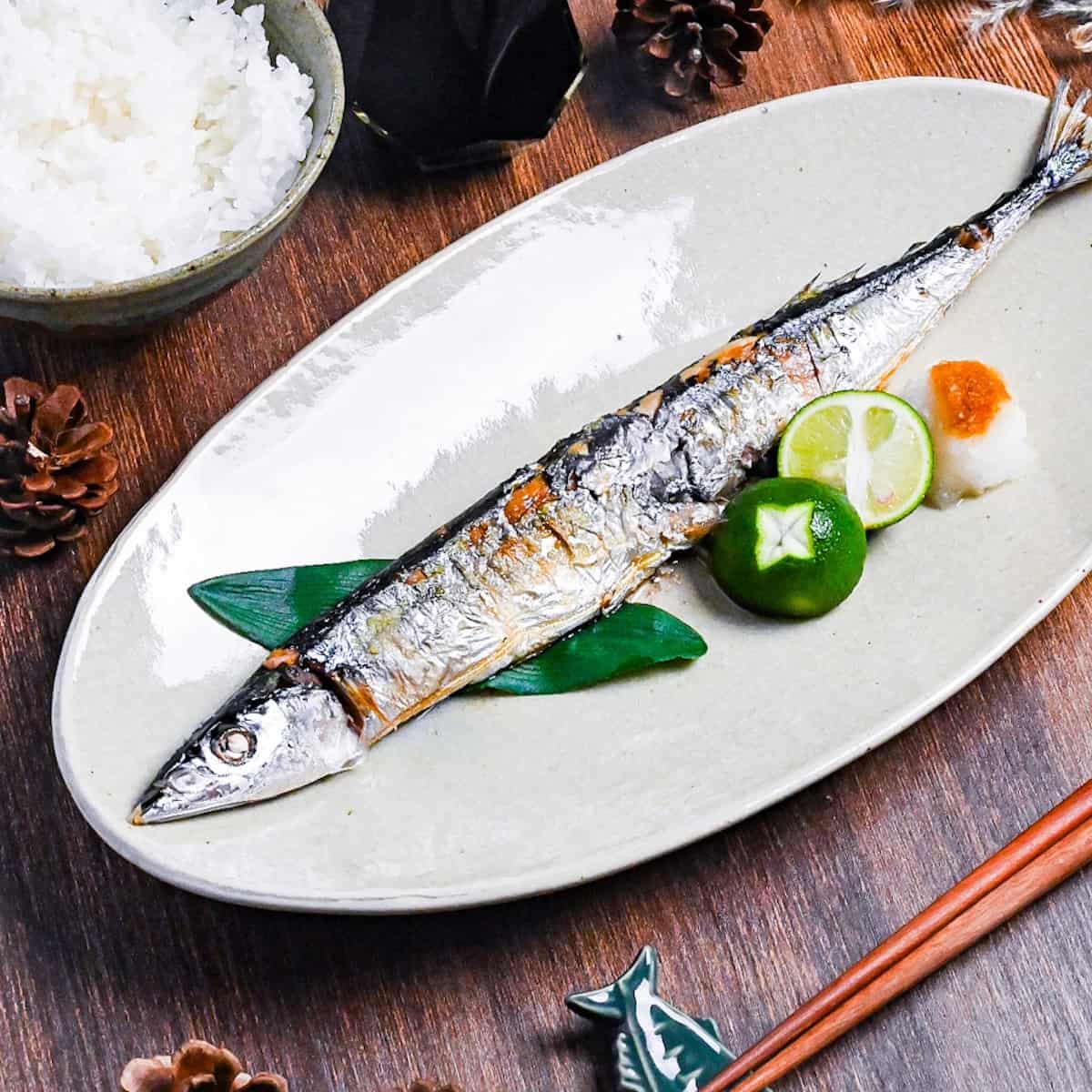 Grilled pacific saury (sanma no shioyaki) on a pale oval plate with grated daikon, sauce sauce and a halved sudachi