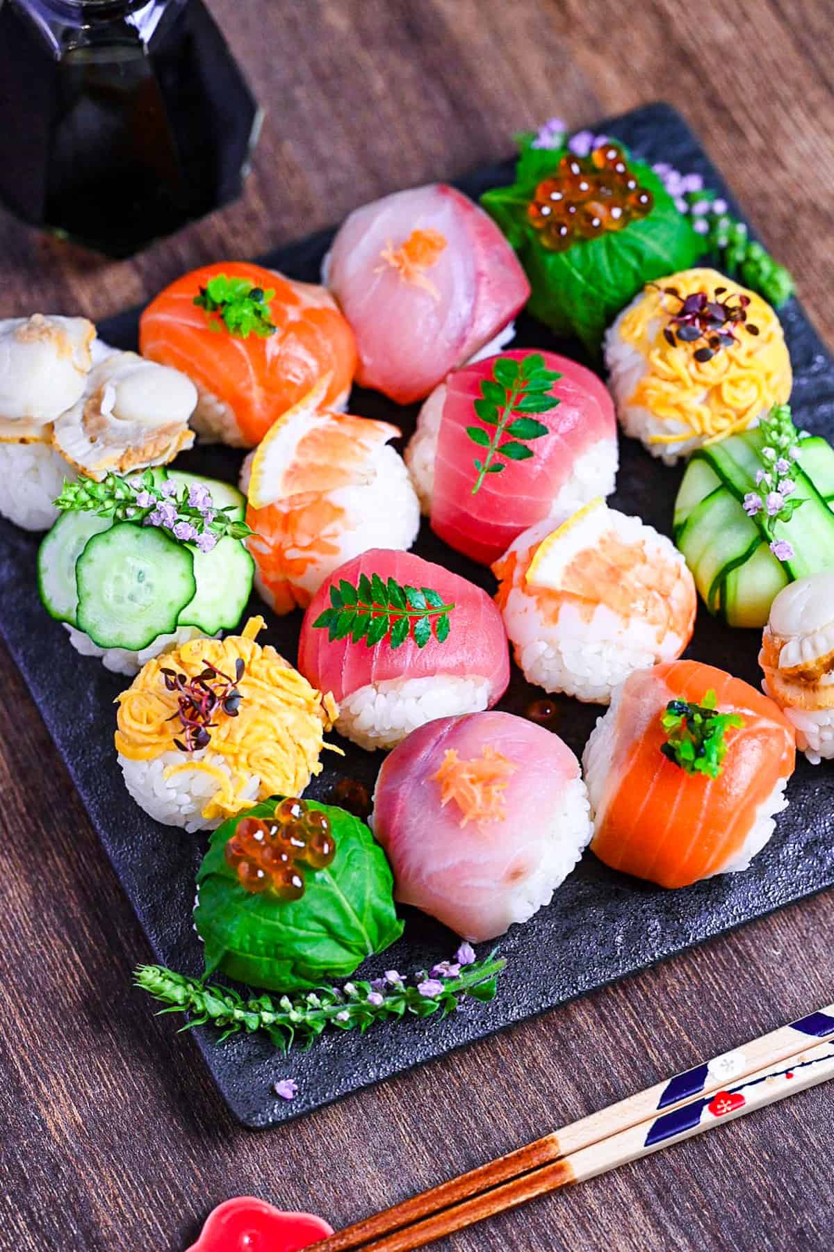 decorative temarizushi made with various seafood, eggs and vegetables topped with leaves, salmon roe, flowers and lemon slices served on a square slate-style plate