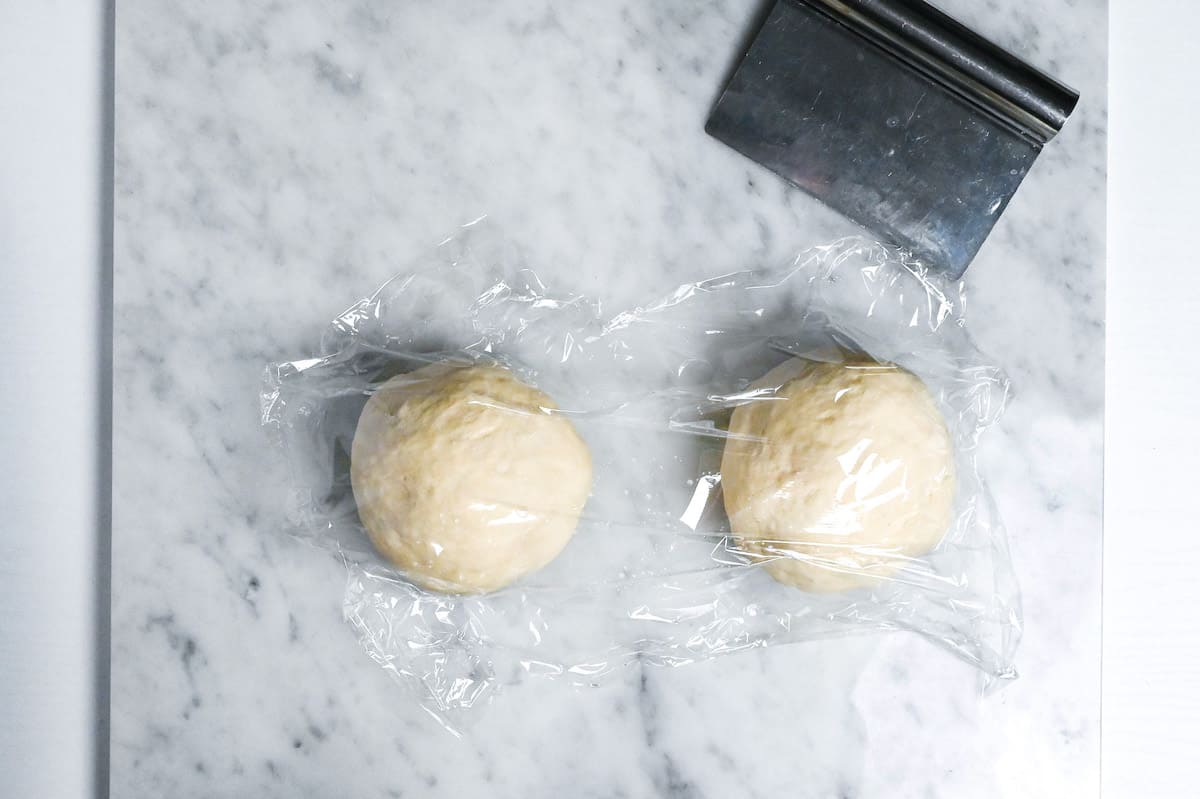 pizza dough cut in two, rolled into balls and wrapped with plastic wrap