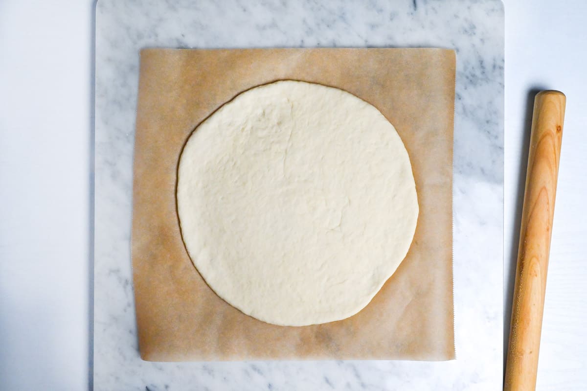 pizza dough rolled out on baking paper