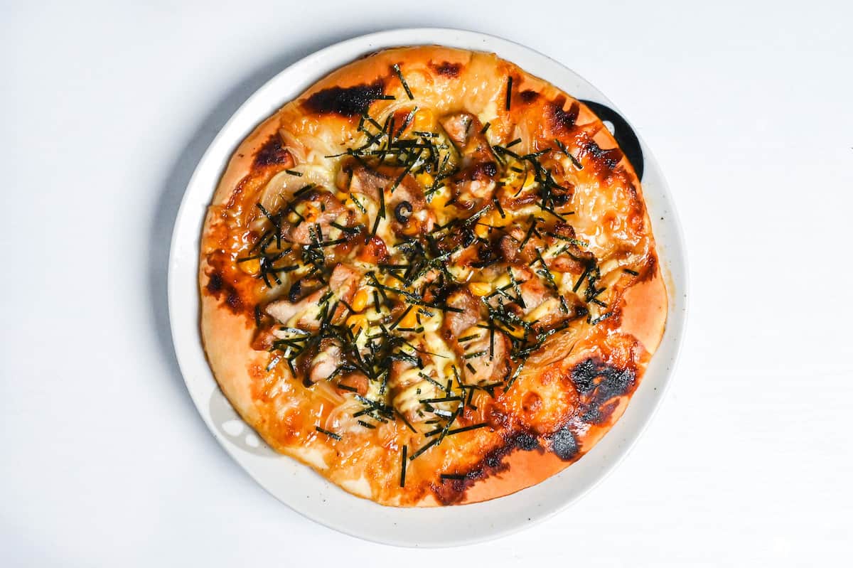 baked teriyaki chicken pizza on a white plate and topped with shredded nori