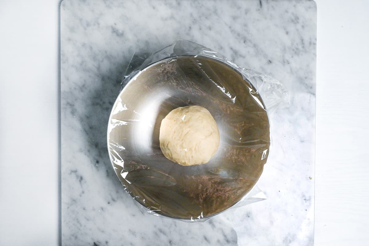 resting dough in a bowl with plastic wrap over the top