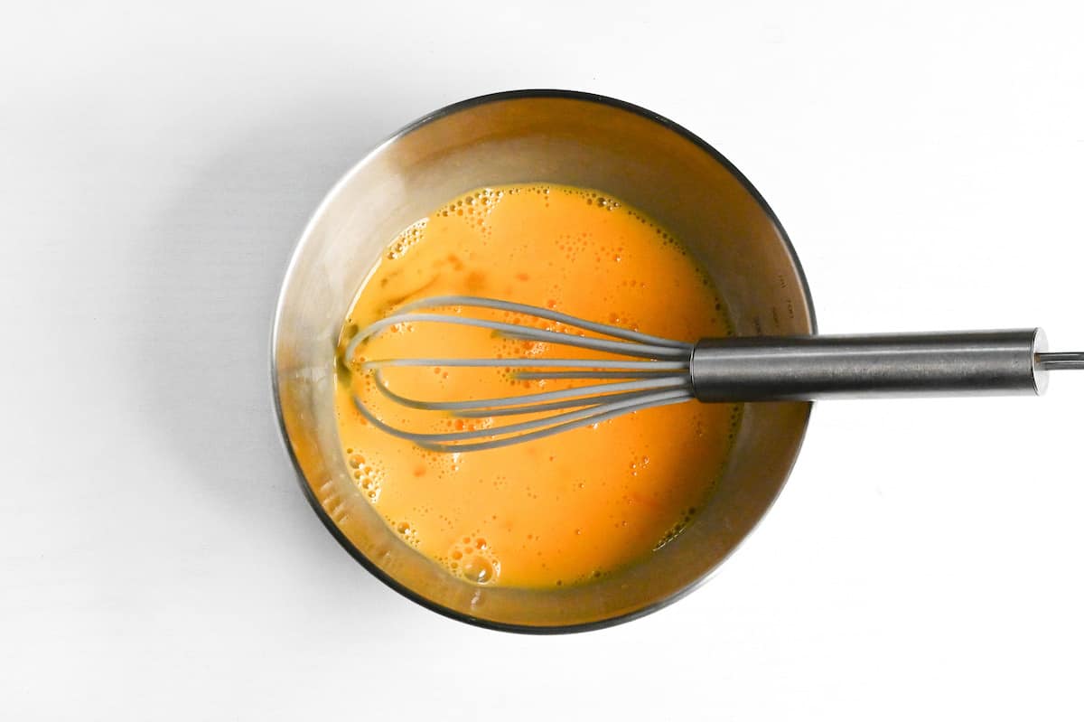 whisked egg in a steel bowl with gray whisk