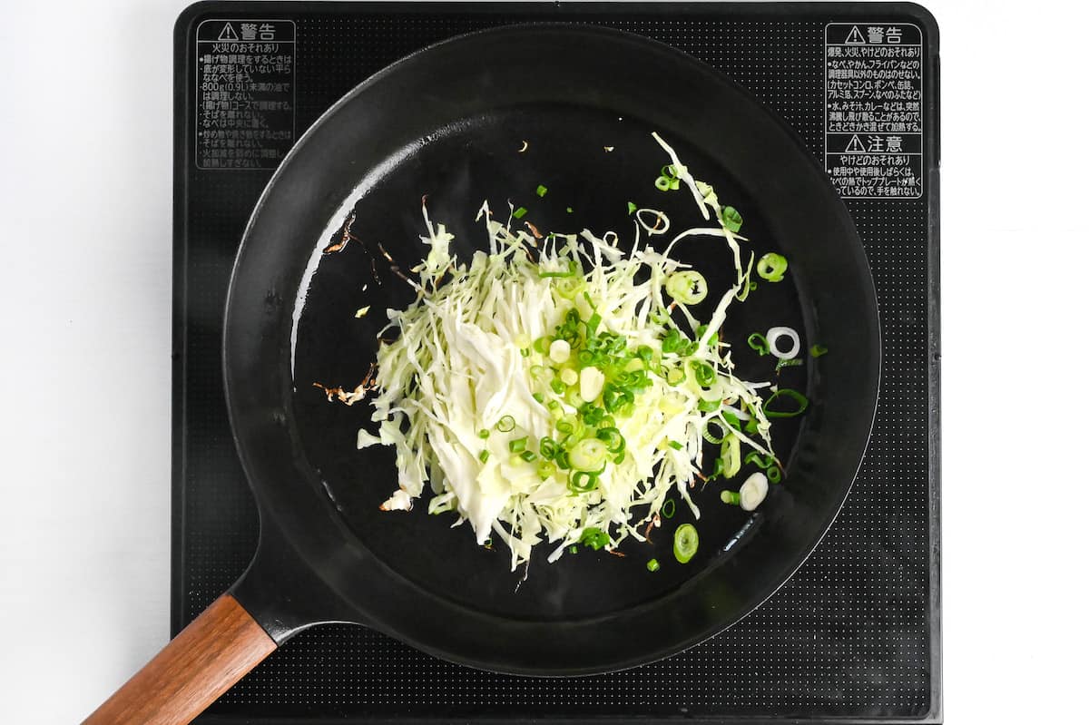 shredded cabbage and finely chopped green onion frying in a frying pan