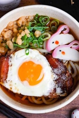 Tsukimi udon made with thick noodles in a dashi broth topped with eggs, bacon, green onion, tempura bits and kamaboko fishcake shaped into a rabbit