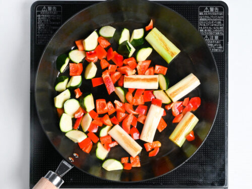 zucchini, green onion and red bell pepper frying in a frying pan