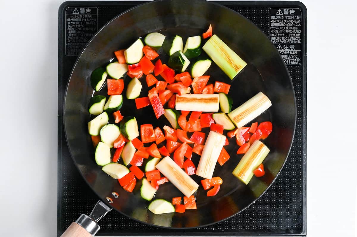 zucchini, green onion and red bell pepper frying in a frying pan