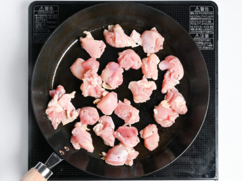 chicken thigh frying in a pan with skin side down