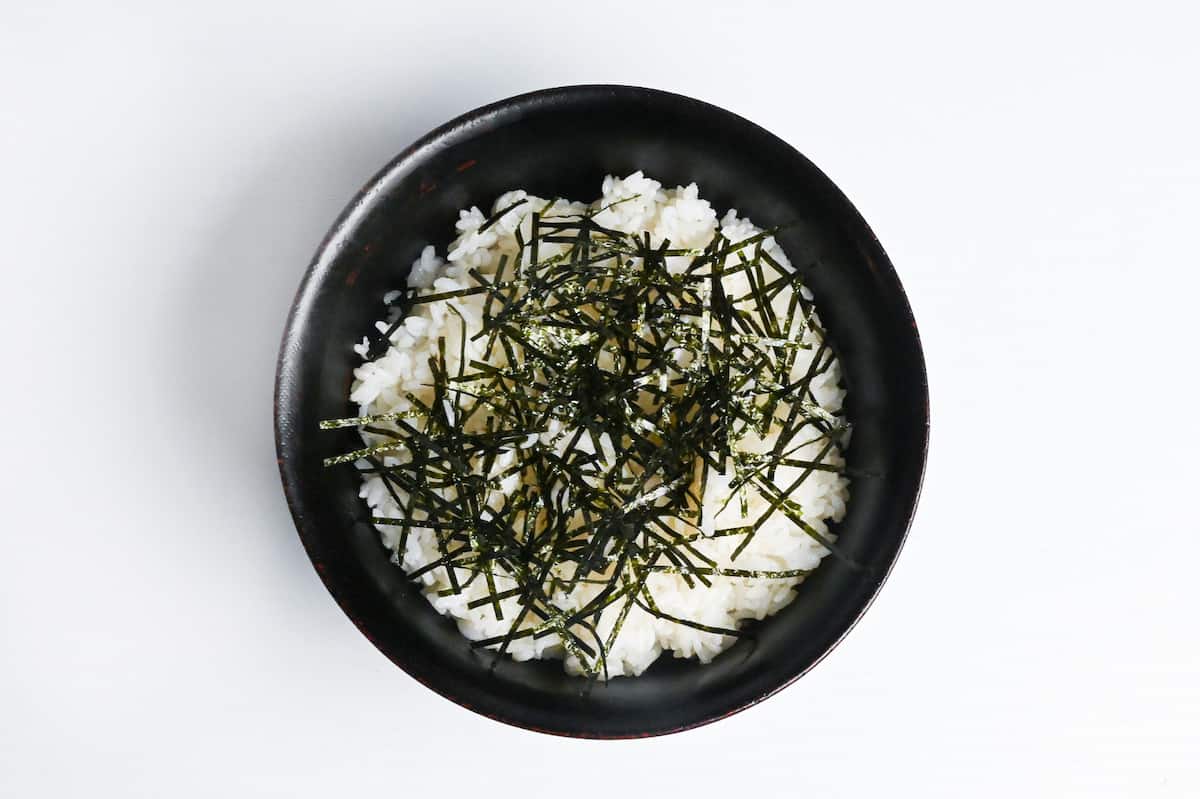 cooked white rice in a black bowl topped with shredded nori seaweed