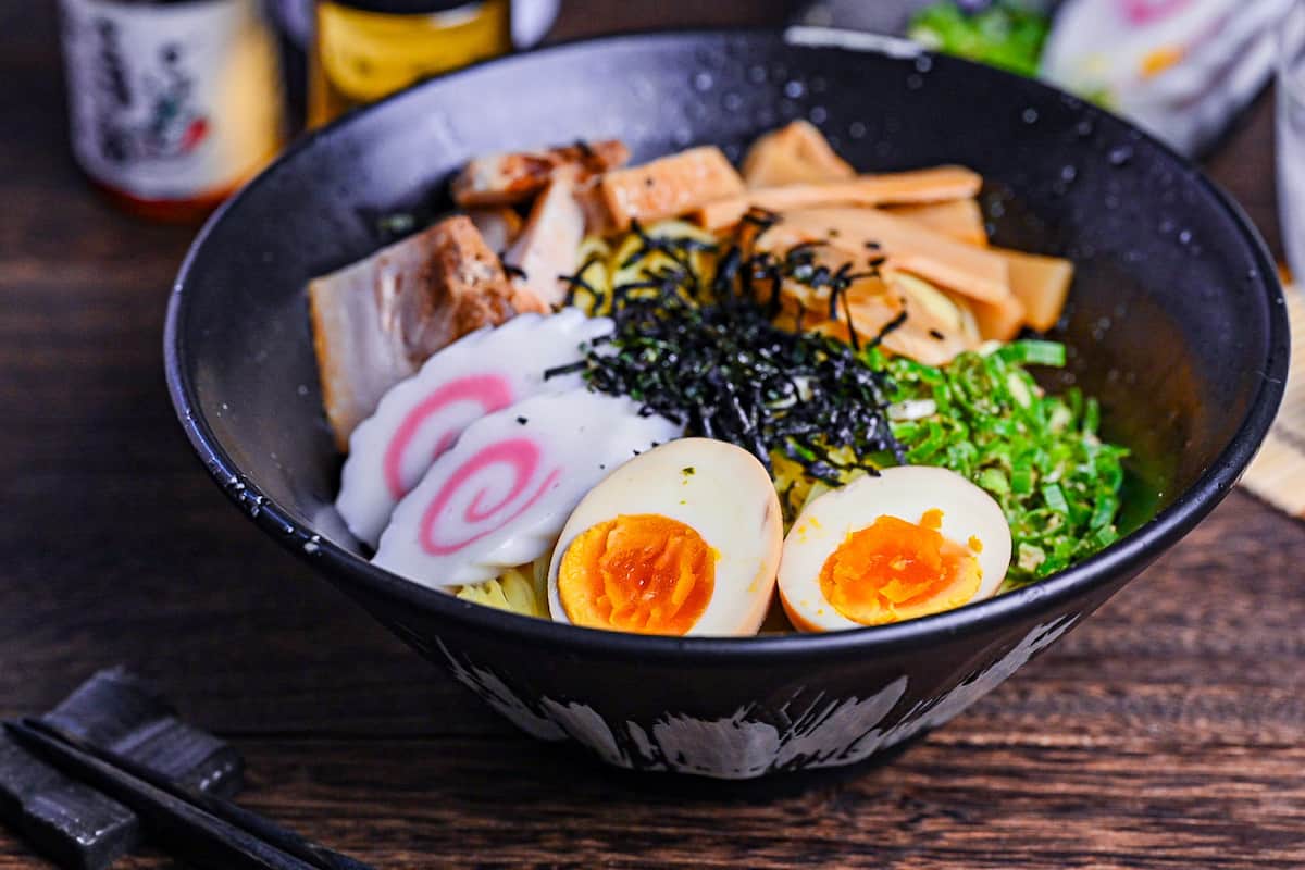 Abura soba soupless ramen in a black bowl topped with ramen egg, narutomaki, menma, chashu, green onion and kizami nori