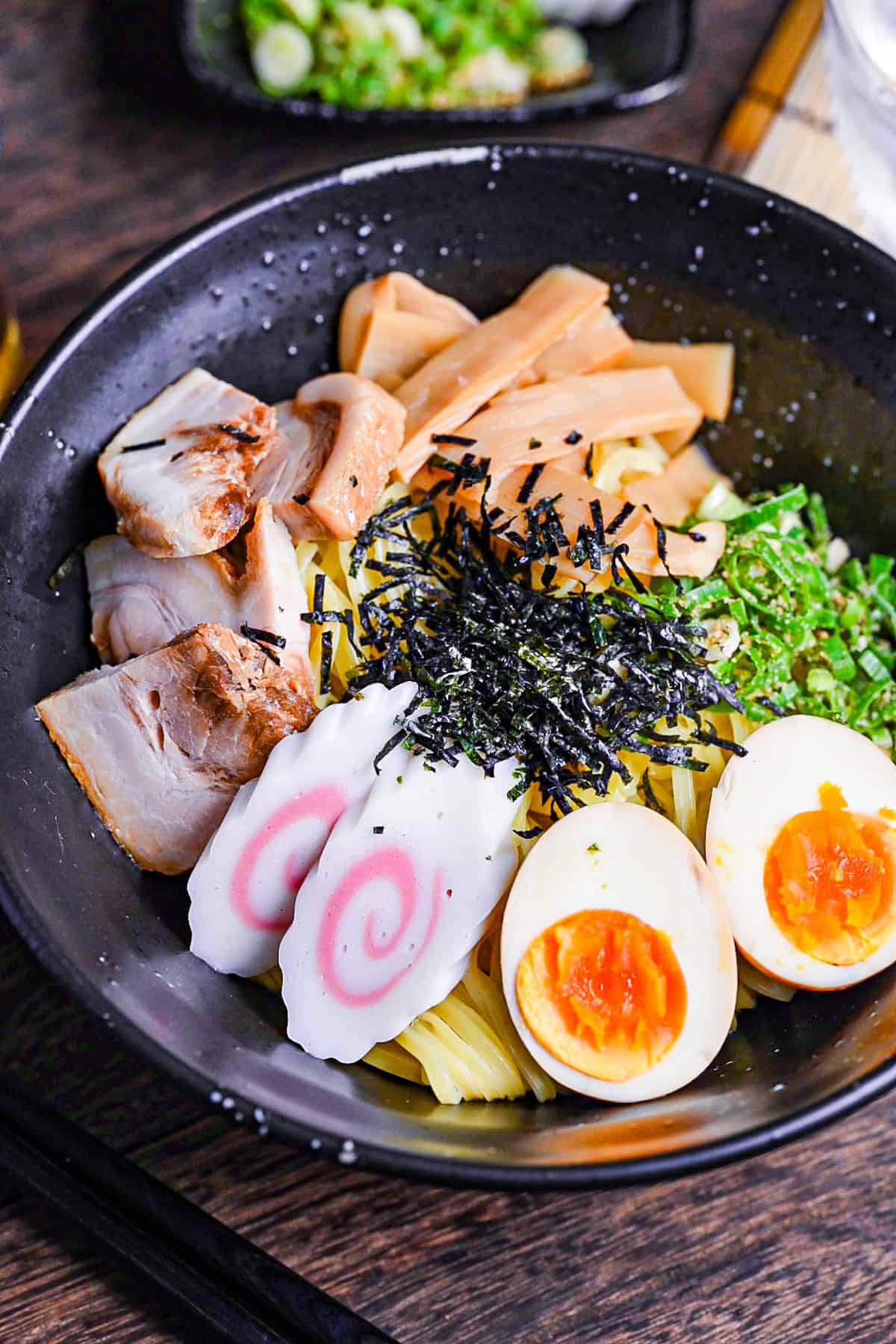 Abura soba soupless ramen in a black bowl topped with ramen egg, narutomaki, menma, chashu, green onion and kizami nori