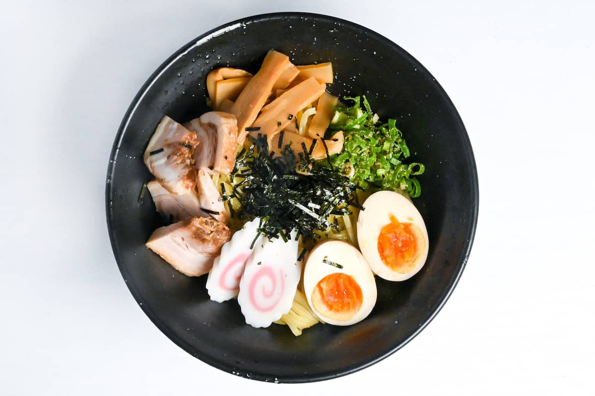 Abura soba soupless ramen in a black bowl topped with ramen egg, narutomaki, menma, chashu, green onion and kizami nori