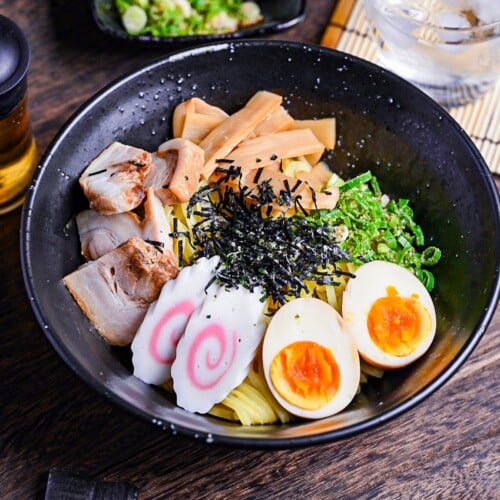 Abura soba soupless ramen in a black bowl topped with ramen egg, narutomaki, menma, chashu, green onion and kizami nori