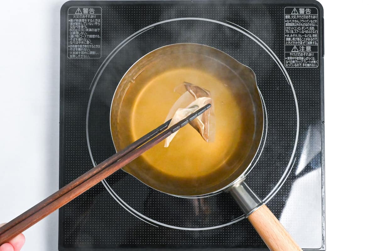 removing dashi packet from saucepan with wooden cooking chopsticks