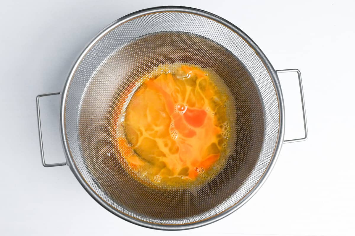 pouring dashimaki tamago egg mixture through a sieve to make it smooth