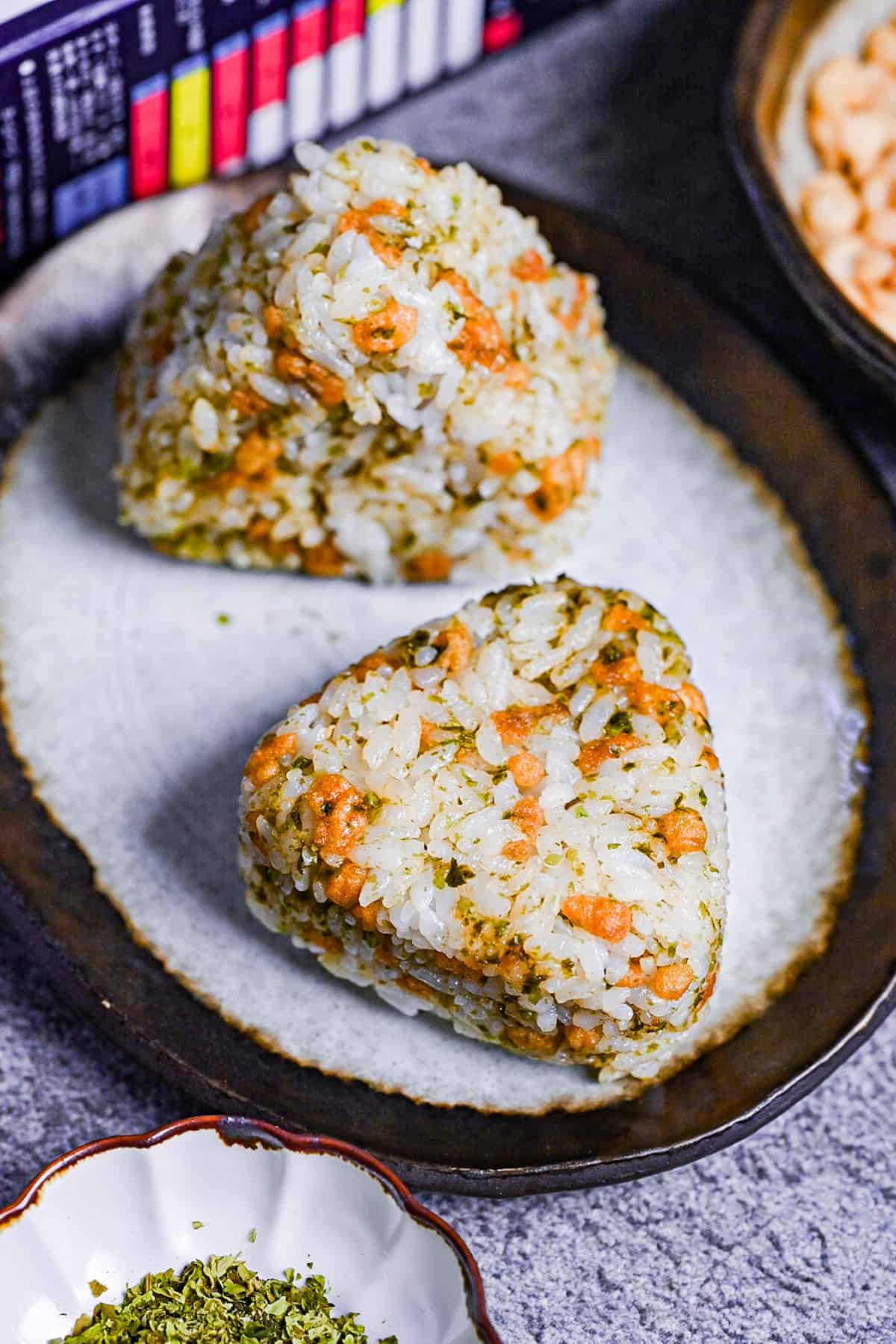 devil's onigiri made with tempura flakes and aonori on a gray plate with a brown border next to a bowl of aonori and tenkasu