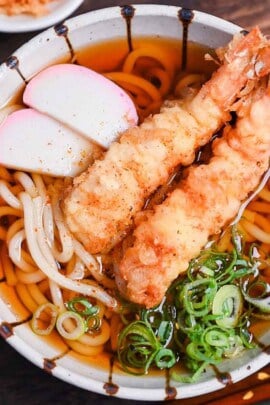 Ebiten Udon - Homemade udon noodle soup in a stripy bowl topped with kamaboko, green onion and tempura shrimp