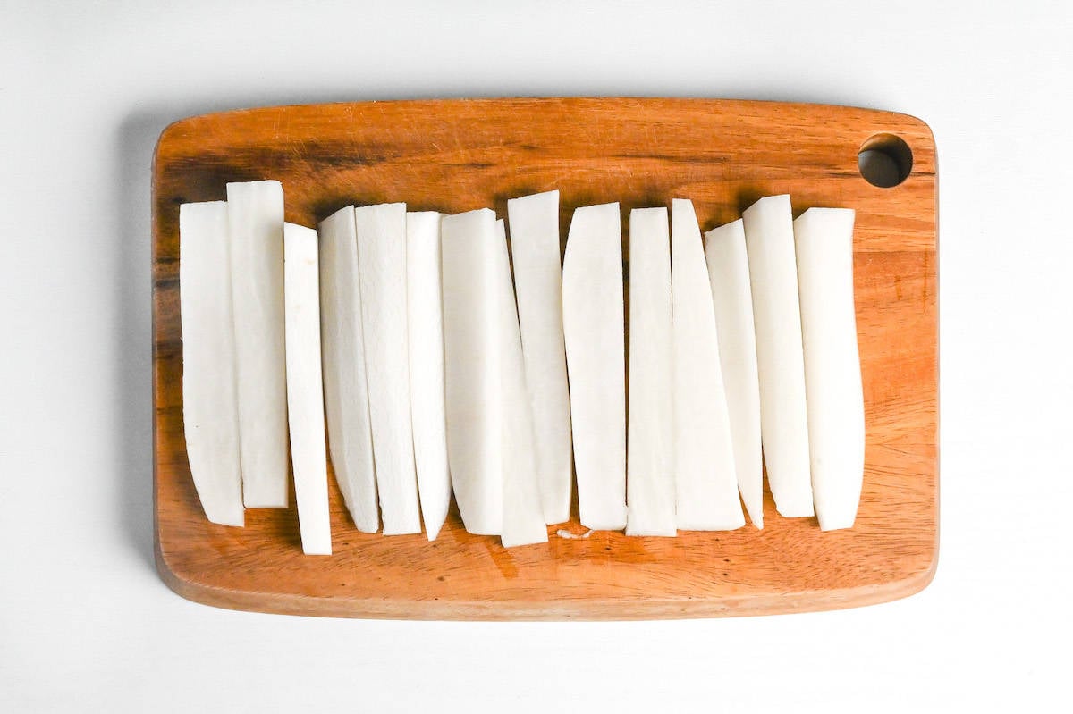 daikon radish cut into strips on a wooden chopping board