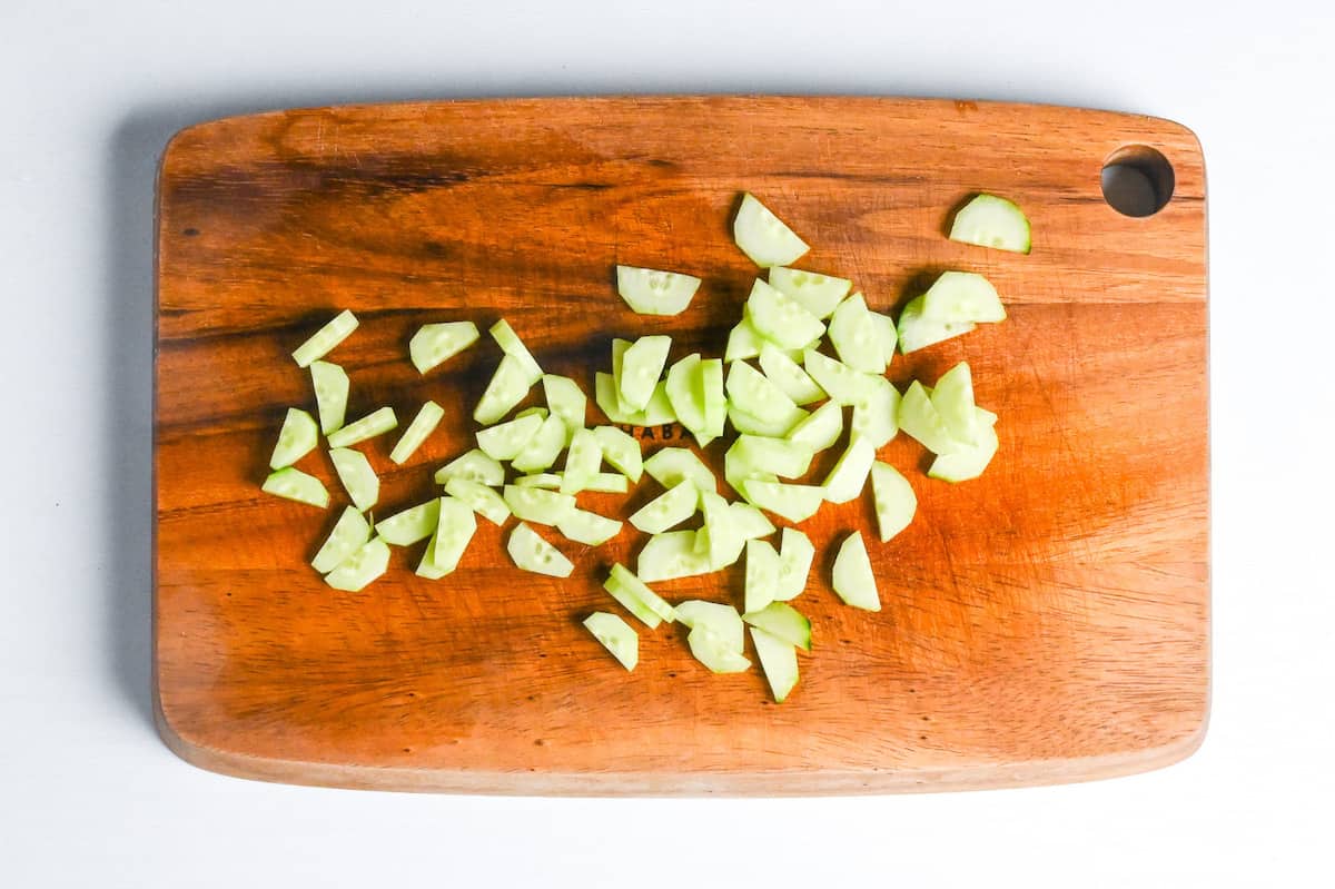 sliced cucumber halves on a wooden chopping board