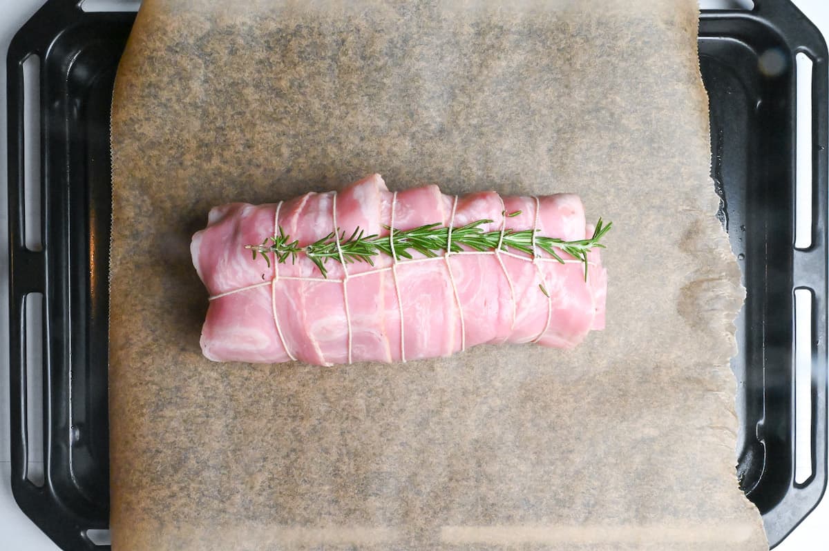 gotcha pork wrapped with butcher's twine and topped with rosemary on a baking tray lined with baking paper
