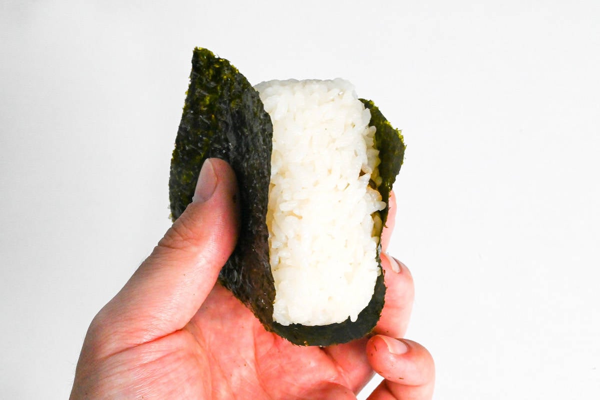 a hand holding kombu onigiri wrapped with nori