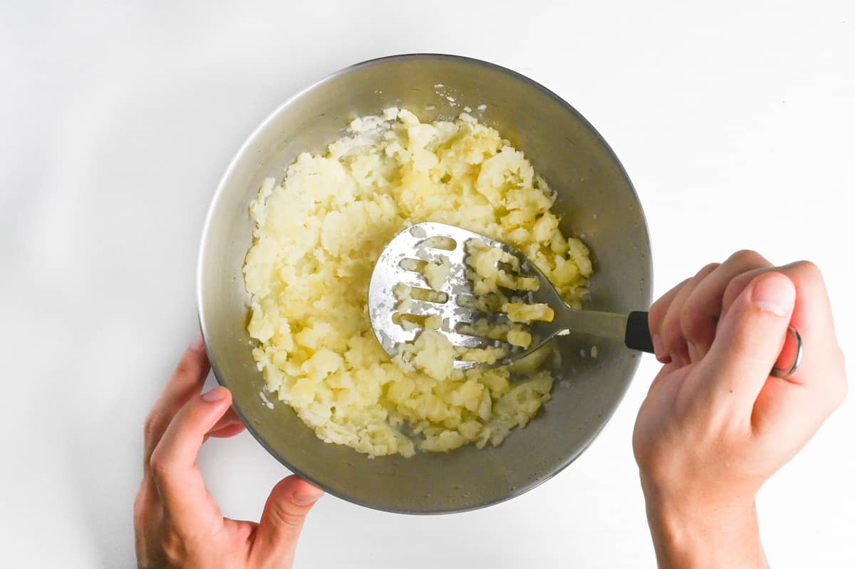 mashing boiled potatoes with milk in a steel mixing bowl