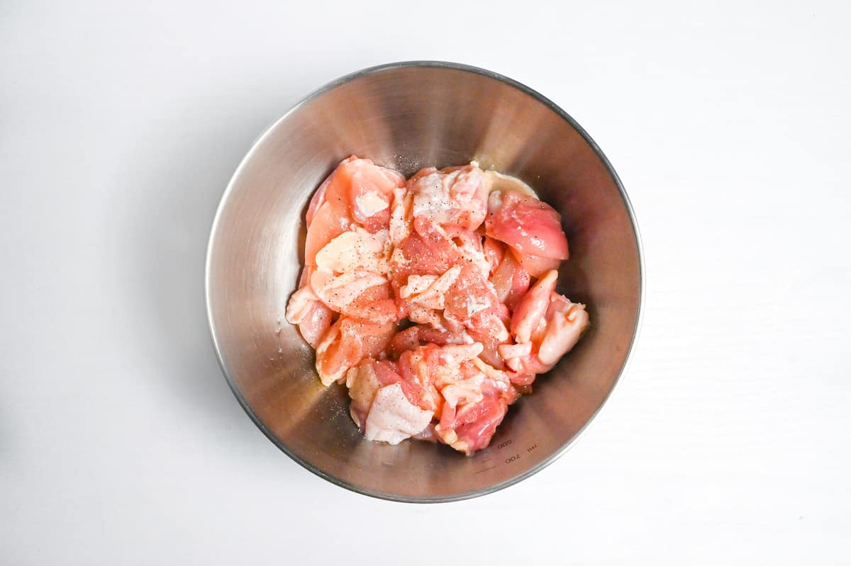 chicken thigh cut into bitesize pieces in a steel mixing bowl with salt and pepper
